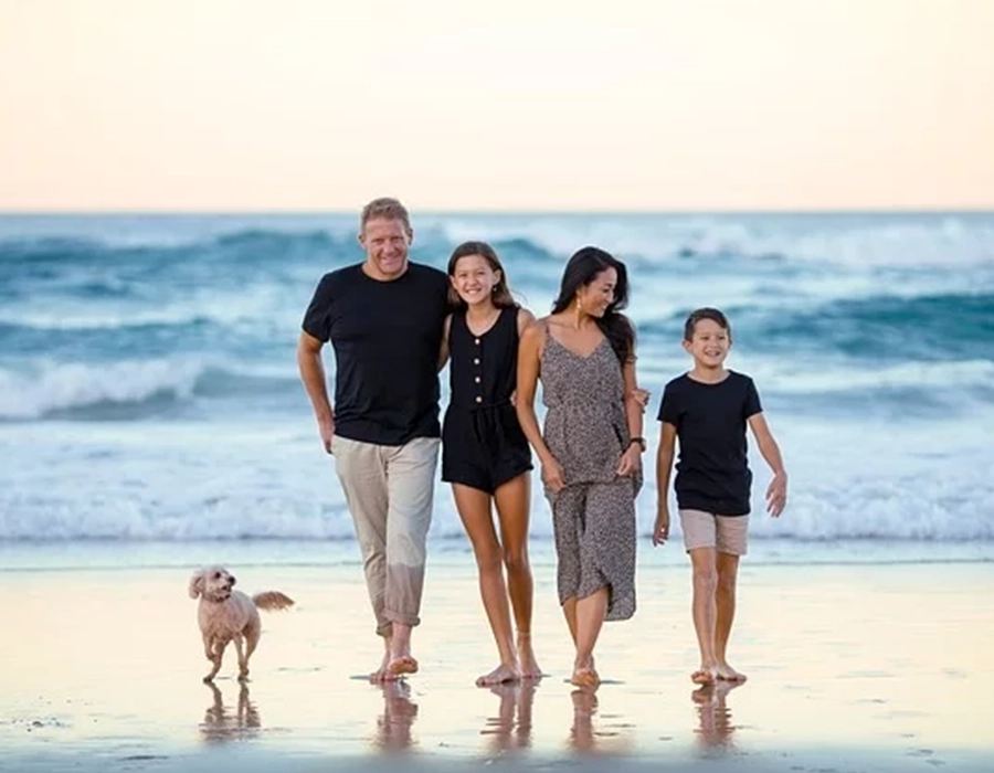 A family of four taking a walk on the beach with their small dog.