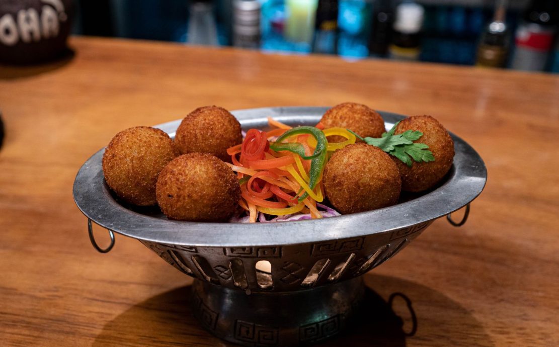 Crispy golden croquettes served on a decorative metal tray with fresh, julienned vegetable garnish at Trader Vic