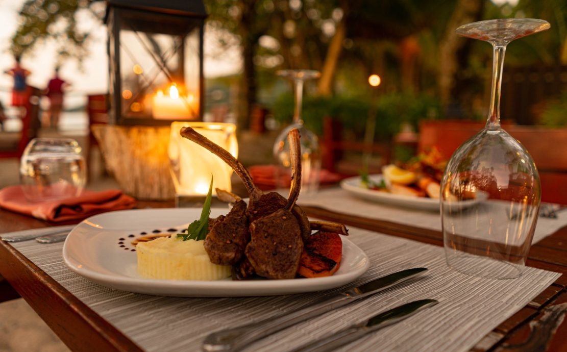 Lamb chops with mashed potatoes, presented on an outdoor table with a lit lantern.