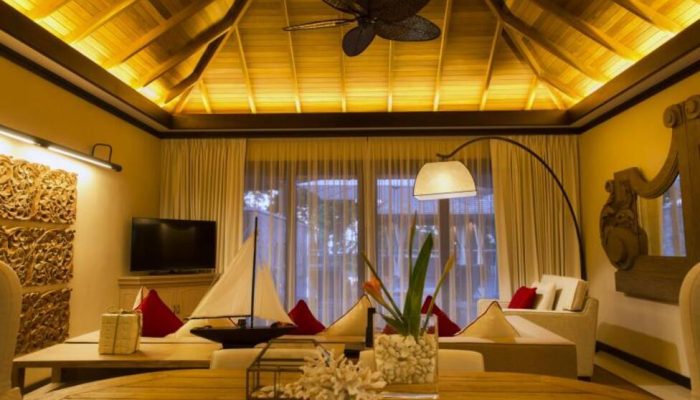 Interior view of a resort suite in the Seychelles featuring high vaulted ceilings with a ceiling fan and cream sofas with red accents.