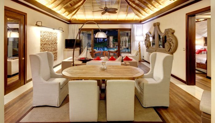 Elegant dining area in a Seychelles resort villa featuring a wooden round table, decorative wall art and ambient lighting.