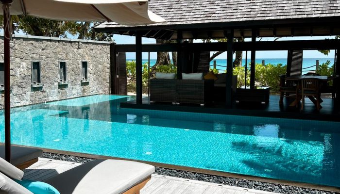 Luxurious outdoor pool in a Seychelles resort with a sun lounger, umbrella, and cabana, surrounded by tropical foliage.