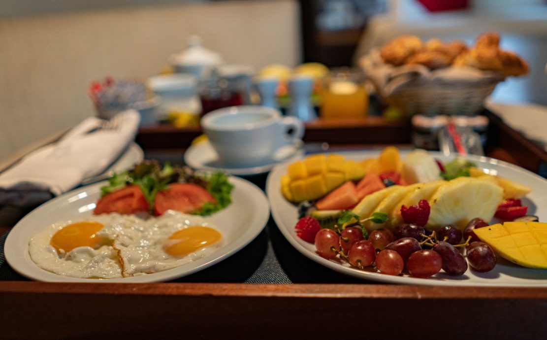 Breakfast tray with eggs, a fruit platter, pastries, and beverages.