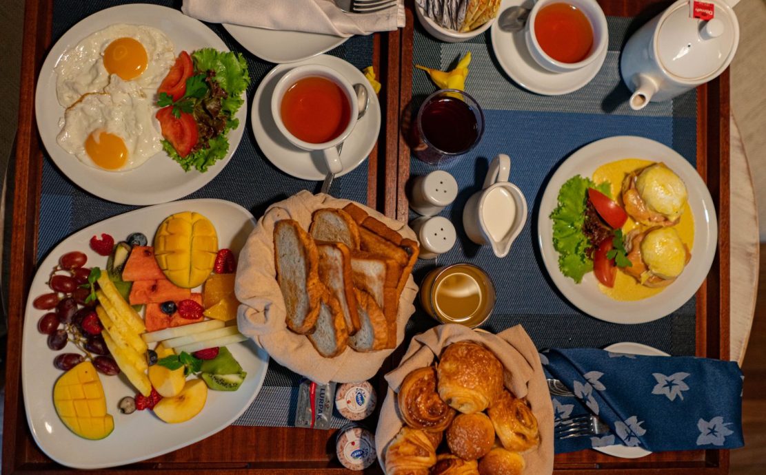 Assorted breakfast dishes with fruits, eggs, pastries, and beverages on a tray.