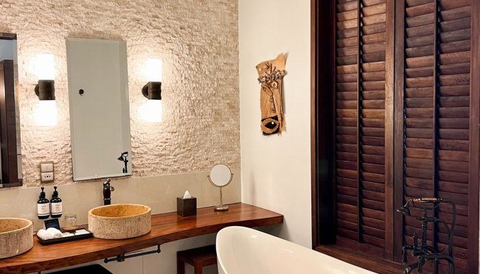 Modern bathroom with a freestanding tub, dual wooden basin vanity, and textured stone walls inside Story Seychelles Resort.