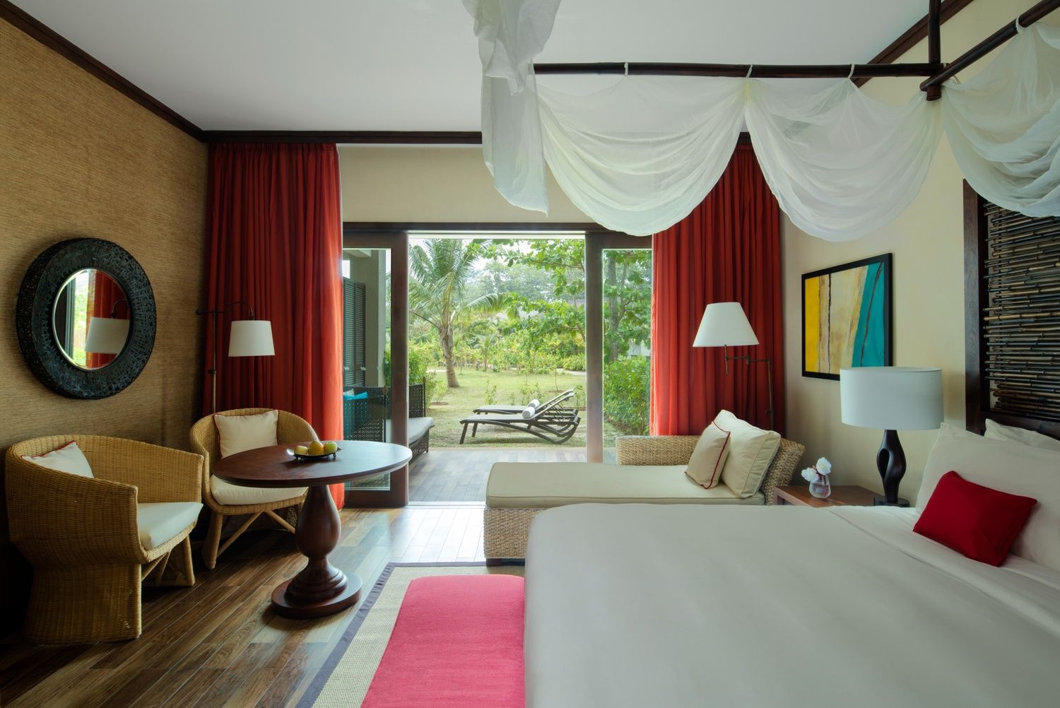 Luxurious resort suite in Seychelles with elegant furnishings, a wide bed with a sheer canopy, and floor-to-ceiling windows offering views of the lush outdoor landscape.