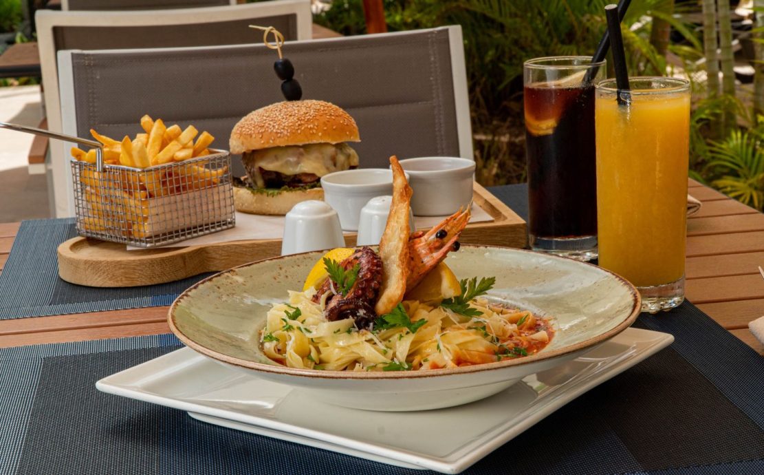 Savory cheeseburger with fries, pasta with seafood, and cold drinks served on a table.