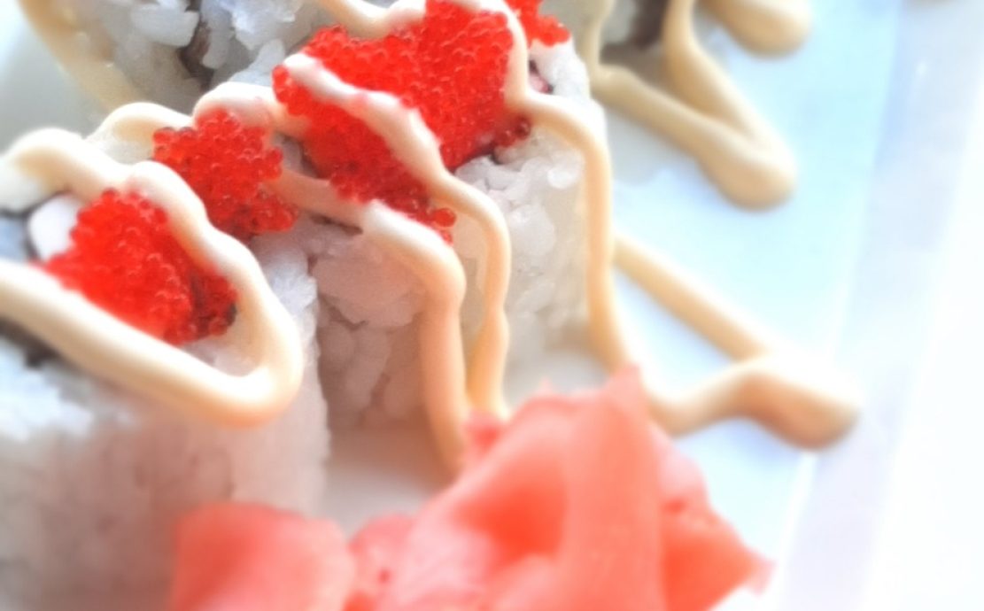 A plate of sushi rolls topped with red tobiko and creamy sauce, accompanied by pickled ginger and wasabi, served at a Seychelles oriental restaurant.