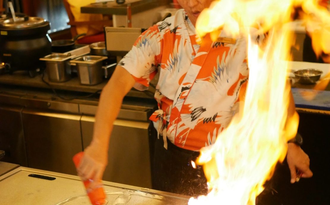 Teppanyaki chef in action, creating a high flame on the grill, in the lively atmosphere of a Seychelles restaurant.
