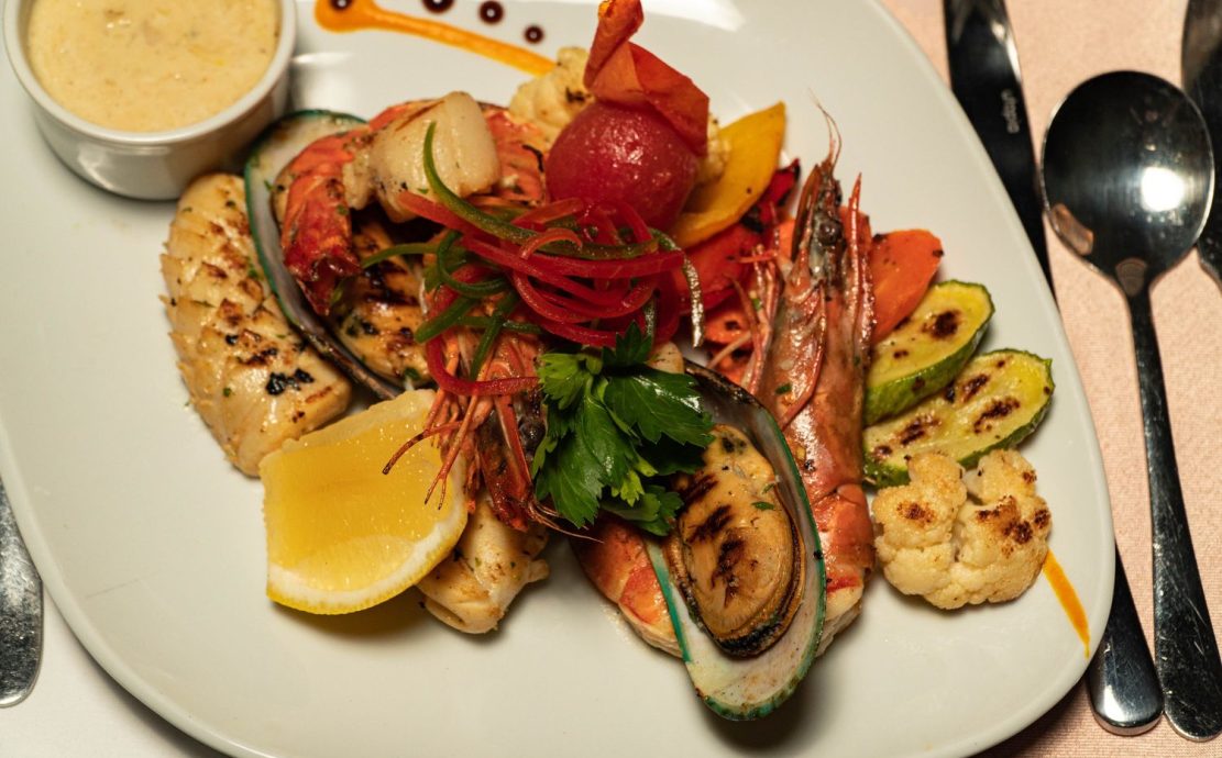 Gourmet seafood platter at a Story Seychelles restaurant, featuring grilled fish, prawns, and vegetables.