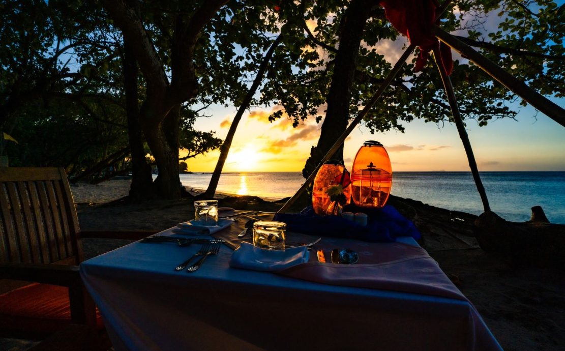 Sunset beach dining setup under trees at Story Seychelles at Beau Vallon Beach.