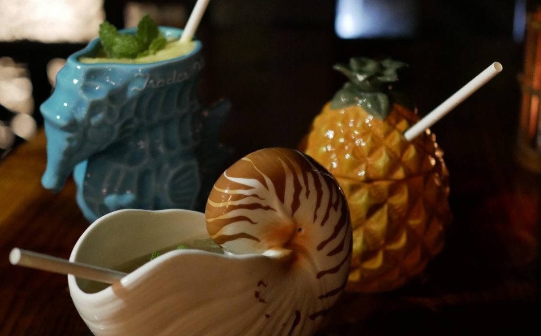 Colorful tiki-themed ceramic mugs in various shapes, including a pineapple and a nautilus shell, filled with tropical drinks, served at Story Seychelles resort in Mahe.