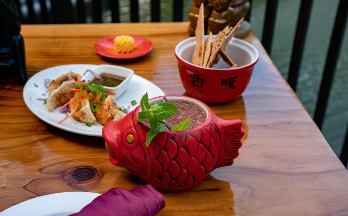 Exotic fish-shaped mug filled with a refreshing mint-topped cocktail, alongside Asian-inspired dishes, at Story Seychelles