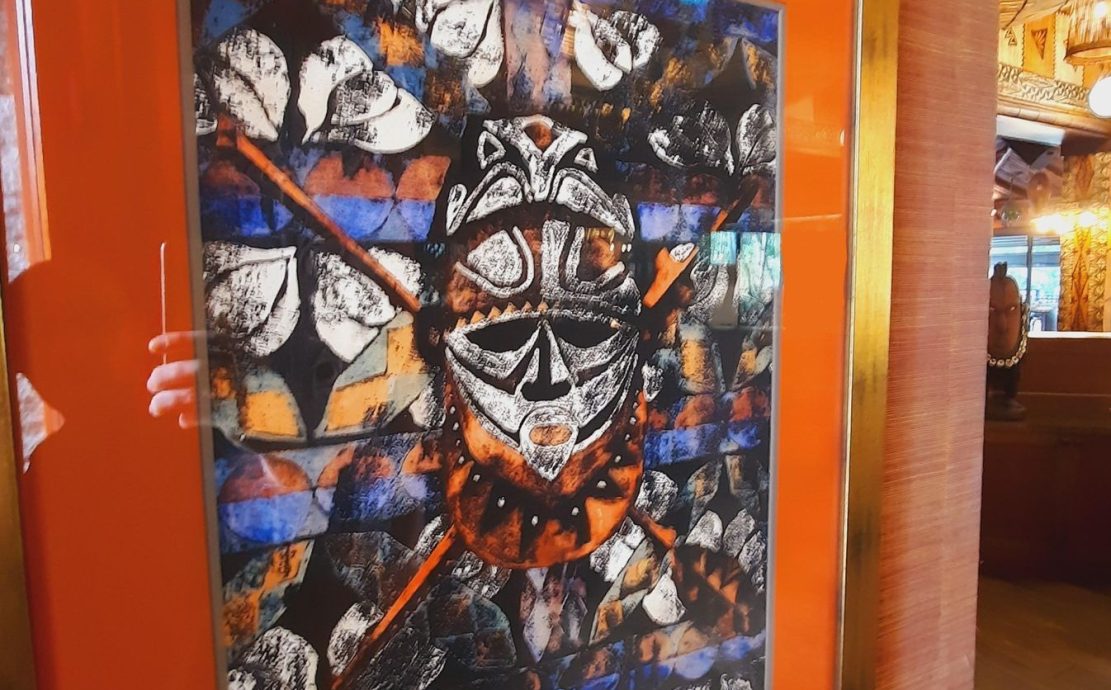 Colorful artwork featuring a tribal mask, displayed in a vibrant orange frame at a resort restaurant in Seychelles.