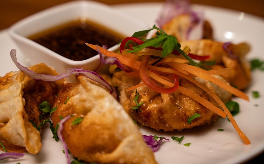 Golden fried samosas garnished with fresh herbs and julienne vegetables, served with a dipping sauce at a Seychelles diner.