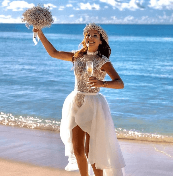 Bride celebrating at a Seychelles wedding on the beach, with a bouquet in hand and the Indian Ocean in the background.