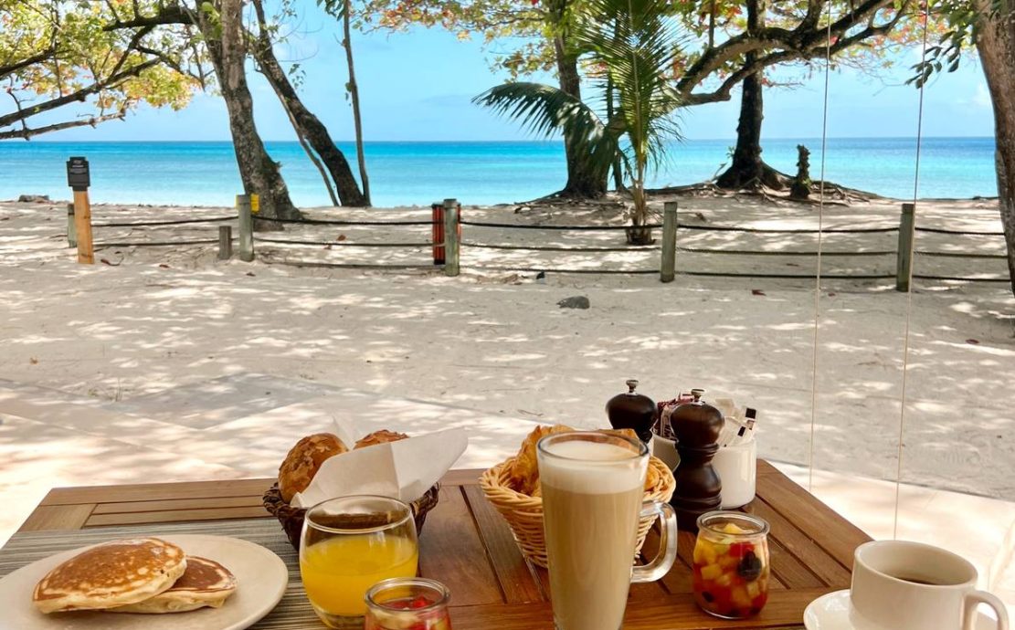 Beachfront breakfast with pancakes, fresh fruit, and coffee, overlooking the serene blue waters at Vascos.