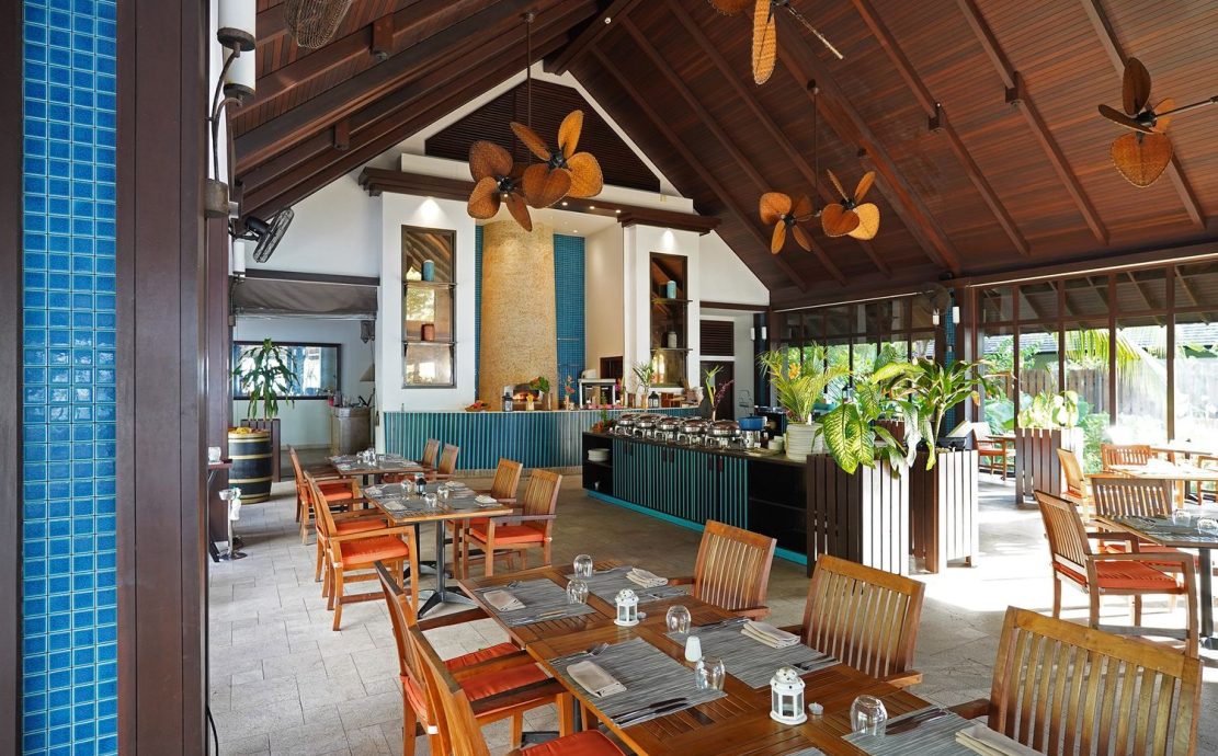 Elegant dining setup at a Seychelles restaurant with wooden tables, tropical decor, and a view of the bar area.