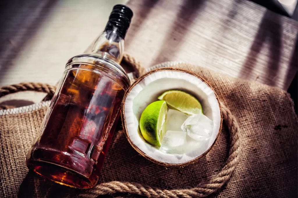 Rum bottle with a fresh coconut drink garnished with lime slices and ice.