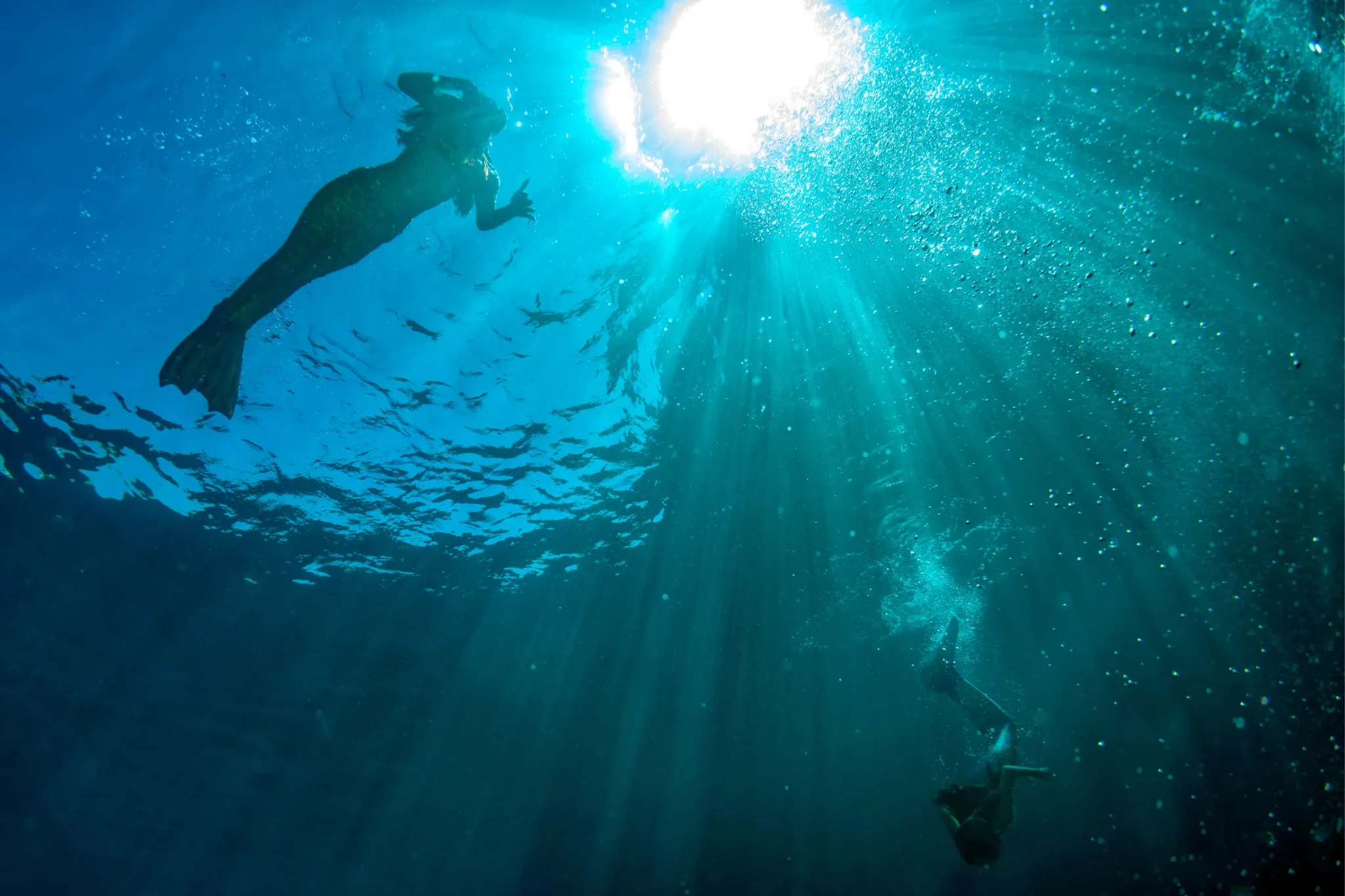 Mermaids swimming underwater in the deep sea.