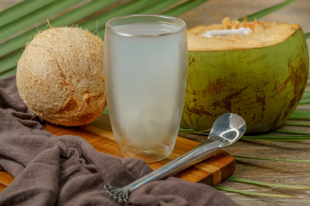 Chilled coconut water in a clear glass beside a freshly opened green coconut.