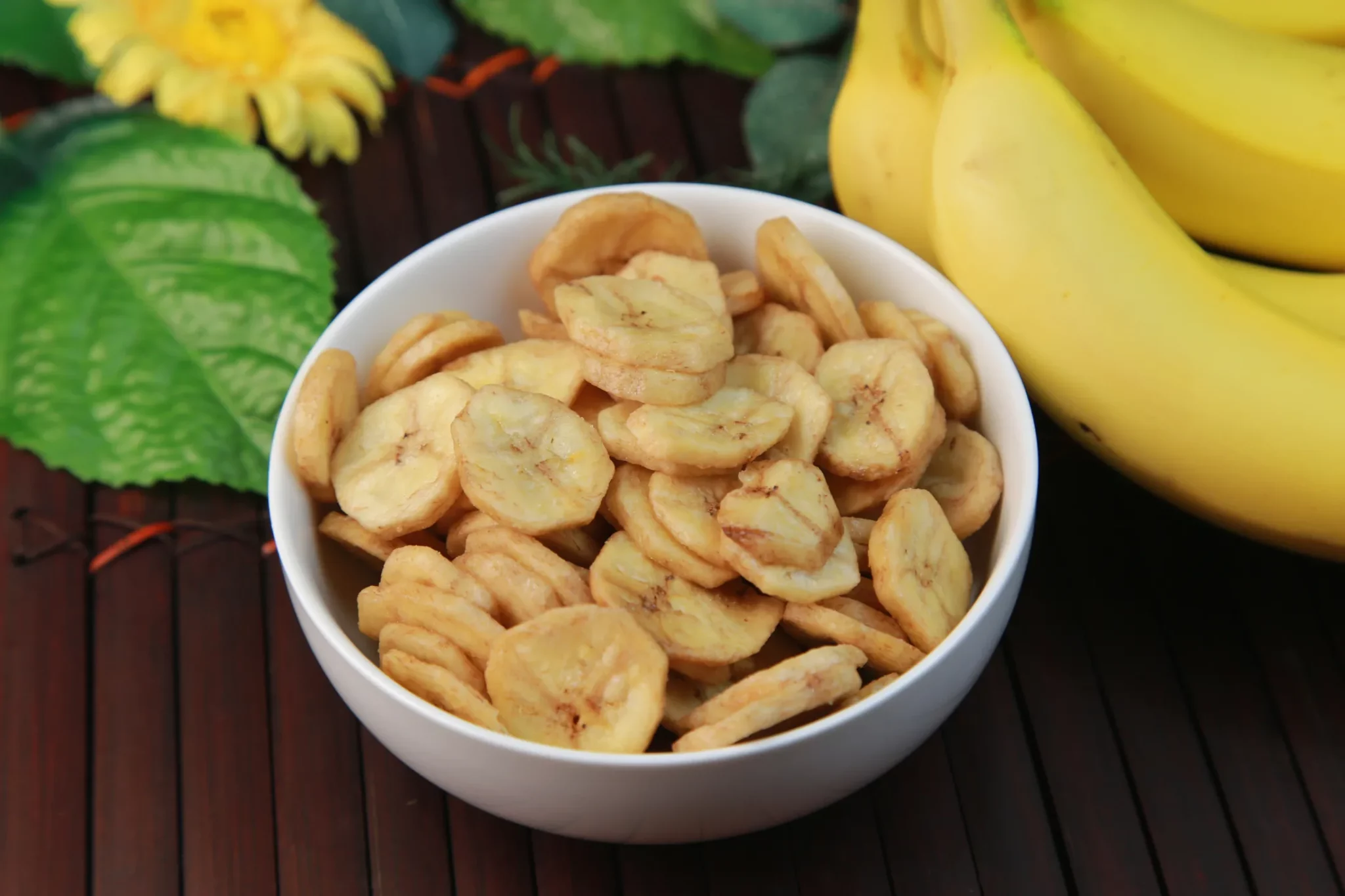 A bowl of banana chips on a wooden table accompanied by fresh bananas, a popular tropical snack in the Seychelles.
