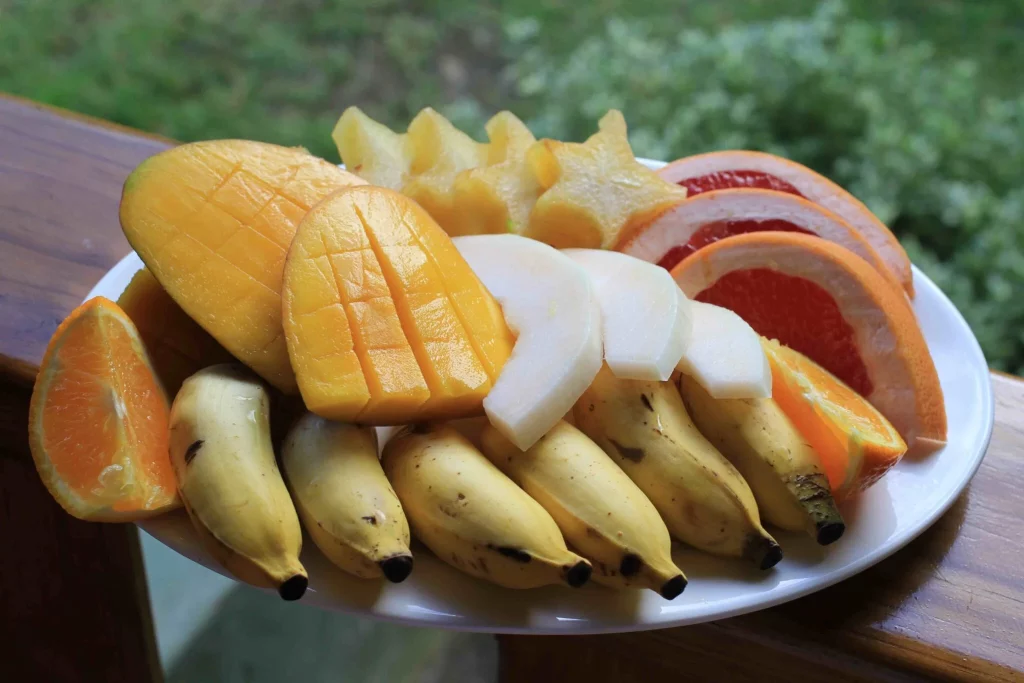 Plate of fresh tropical fruits, including sliced mango, oranges, bananas, and star fruit.