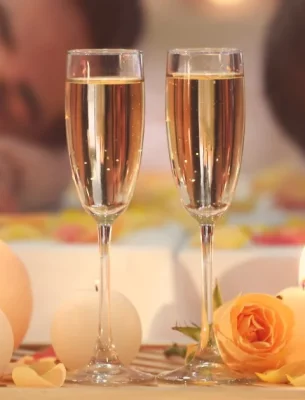 Two champagne glasses next to some candles on a wooden table in front of a couple.