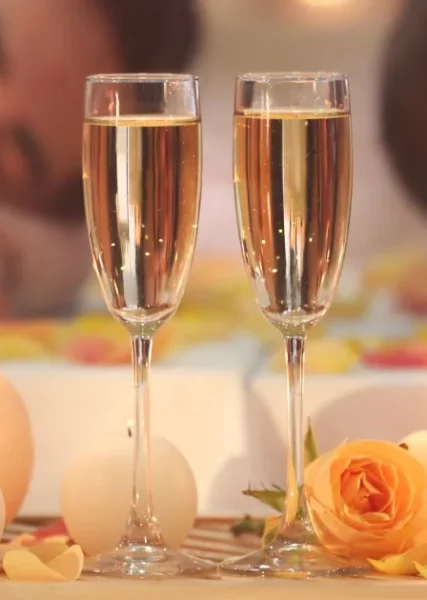 two champagne glasses next to some candles on a wooden table in front of a couple