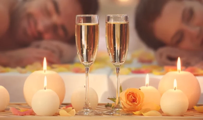 Two champagne glasses next to some candles on a wooden table in front of a couple.