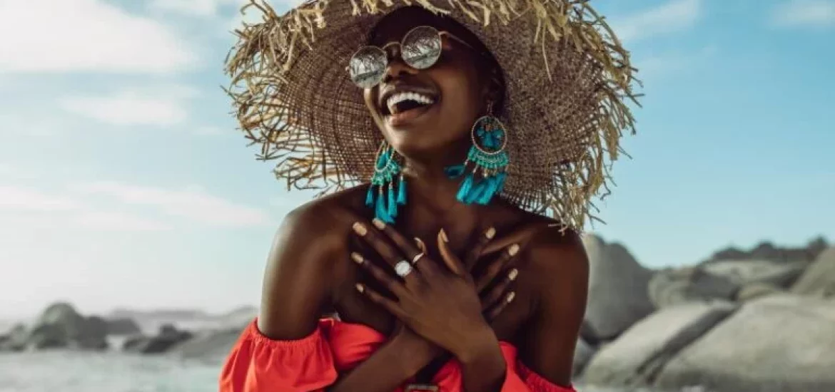 A joyful woman in a wide-brimmed straw hat and reflective sunglasses enjoys the beach.