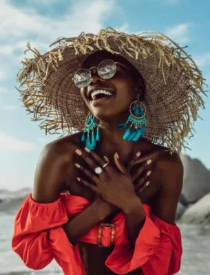 A joyful woman in a wide-brimmed straw hat and reflective sunglasses enjoys the beach.