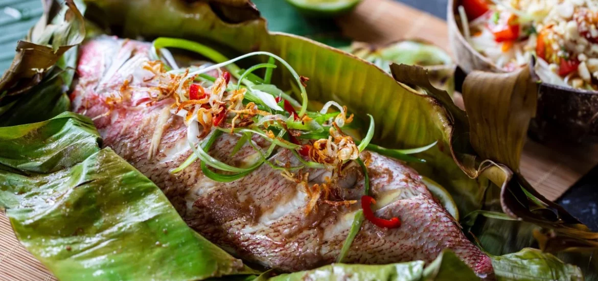 Traditional Seychelles cuisine featuring a freshly prepared fish wrapped in banana leaves, garnished with spices and herbs.