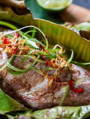 Traditional Seychelles cuisine featuring a freshly prepared fish wrapped in banana leaves, garnished with spices and herbs.