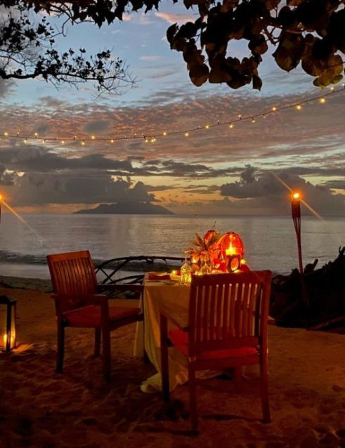 Romantic beachside dining setup at dusk with fairy lights and torches, part of a Seychelles beach resort experience.