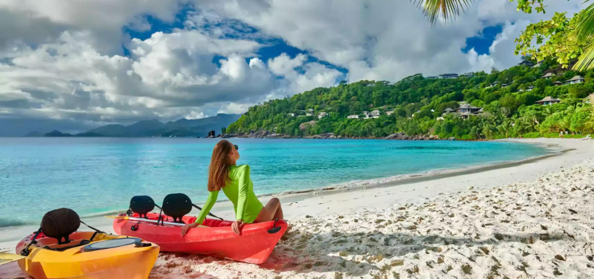 Woman sitting on a red canoe next to a yellow one on a beach at the Seychelles.