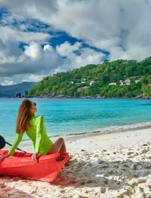 Woman sitting on a red canoe next to a yellow one on a beach at the Seychelles.