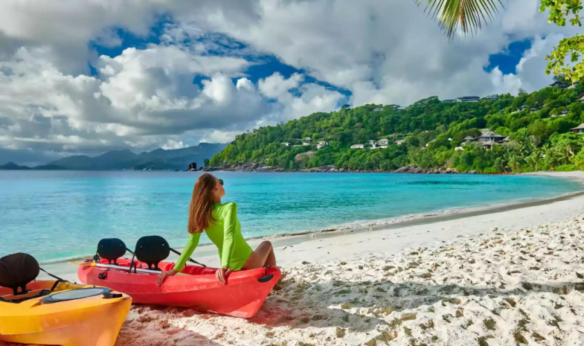 Woman sitting on a red canoe next to a yellow one on a beach at the Seychelles.