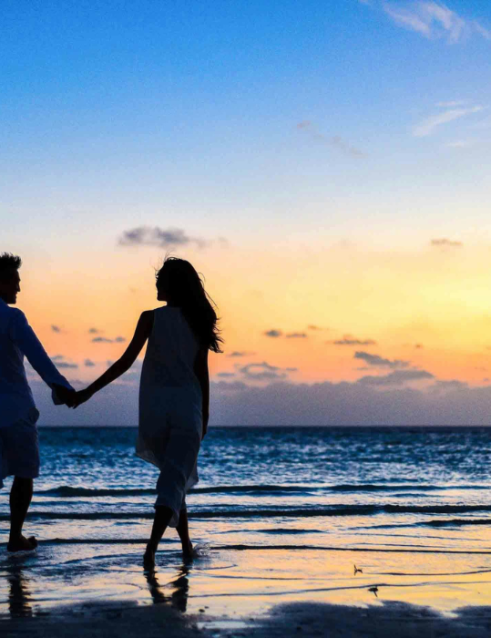 Silhouette of a couple holding hands on the beach at sunset, a romantic Seychelles honeymoon destination.