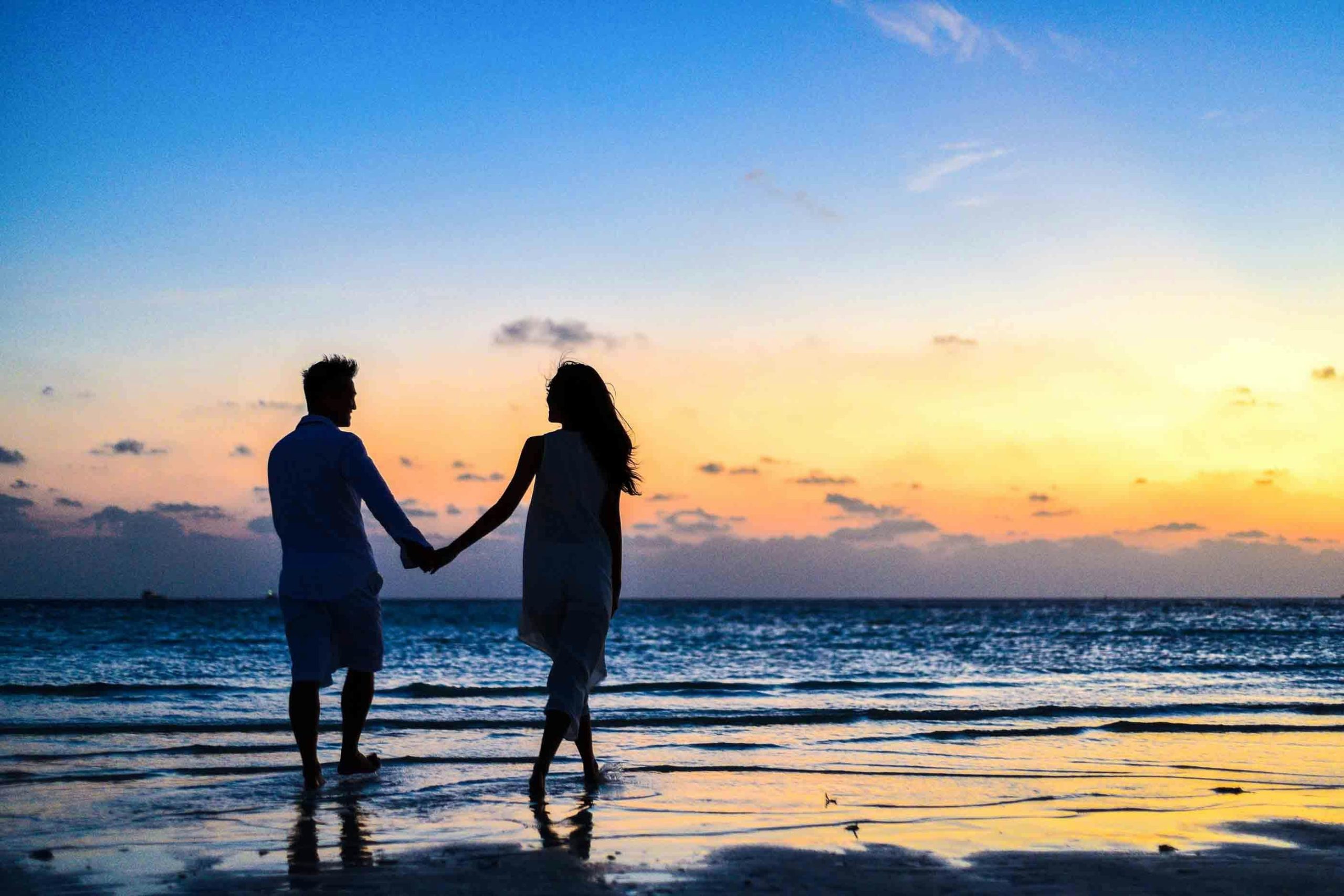 Silhouette of a couple holding hands on the beach at sunset, a romantic Seychelles honeymoon destination.