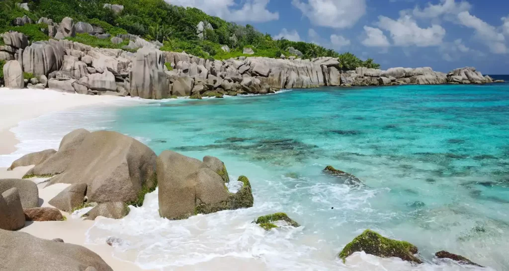 White sand beach meets crystal-clear water between weathered granite formations at Anse Marron, La Digue