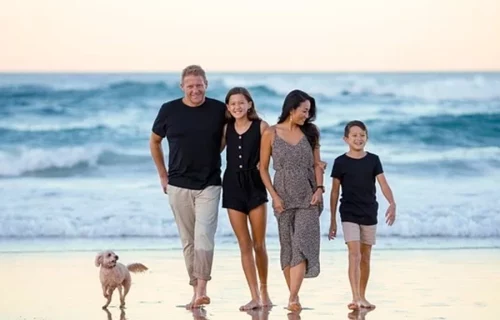 A family of four taking a walk on the beach with their small dog.