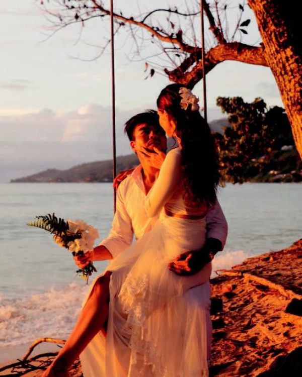 A couple in a romantic embrace on a beach at sunset, on their honeymoon in Seychelles.